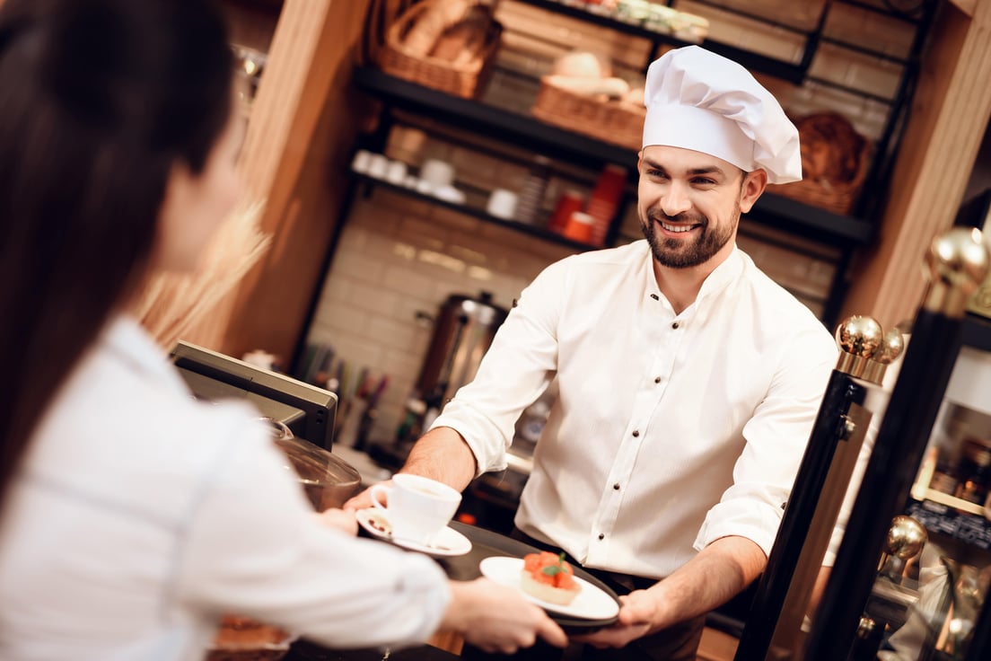 young-man-selling-cakes-and-tea-to-woman-in-bakery-min